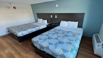 A hotel room with two beds, a wooden floor, a wall-mounted air conditioner, and a ceiling light fixture.