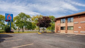 A 6 Motel with a clear sky, a parking lot, and a brick building. - 2 Queen Beds|Mobility|Tub|Nsmk (East Syracuse)