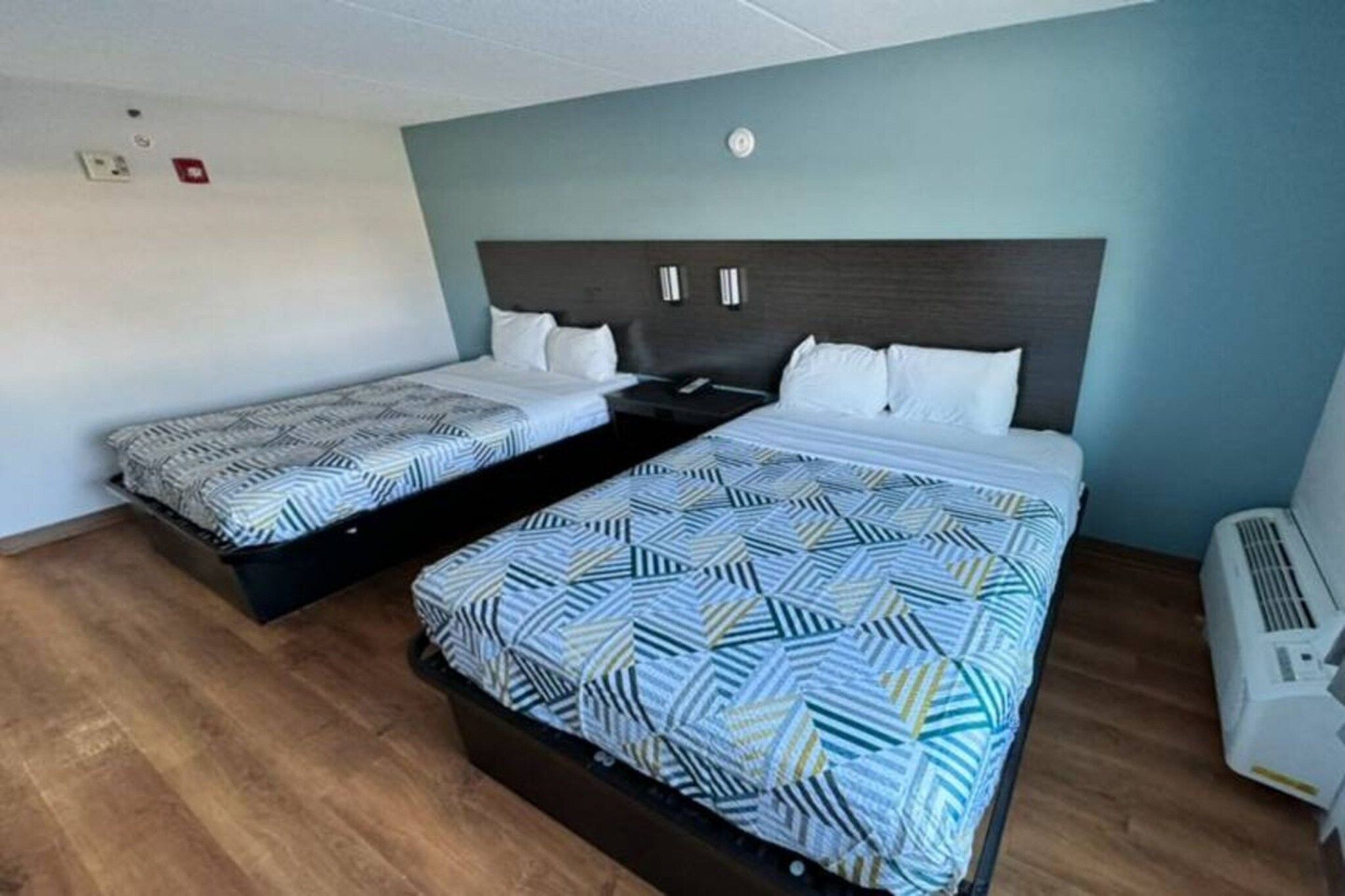 Habitación de hotel con dos camas, piso de madera, aire acondicionado de pared y lámpara en el techo.
