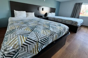 Ein Hotelzimmer mit einem großen Bett, einem kleineren Bett und einem Nachttisch mit einer Lampe.