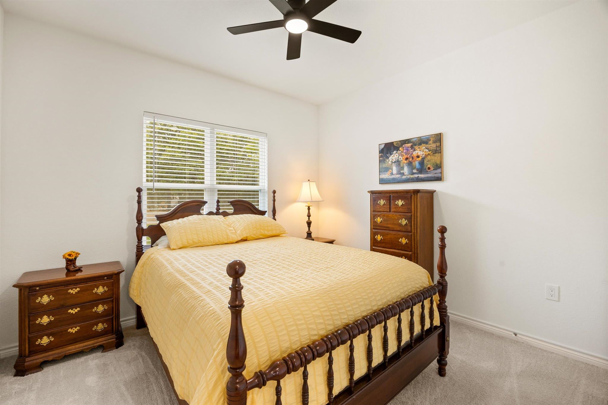 A bedroom with a bed, a nightstand, a dresser, a ceiling fan, and a window with blinds.