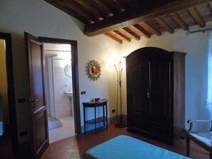 A room with a bed, a wardrobe, a small table, a floor lamp, and a door leading to a bathroom. - Holiday Home in Palaia With Swimming Pool (Palaia)