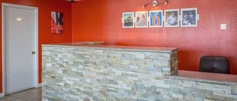 Zona de recepción con mostrador de piedra, puerta blanca y pared roja con cuadros enmarcados.