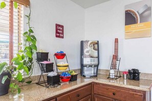 Una estación de café con una máquina de café, un letrero que indica los horarios de café y diferentes recipientes para café y bocadillos.