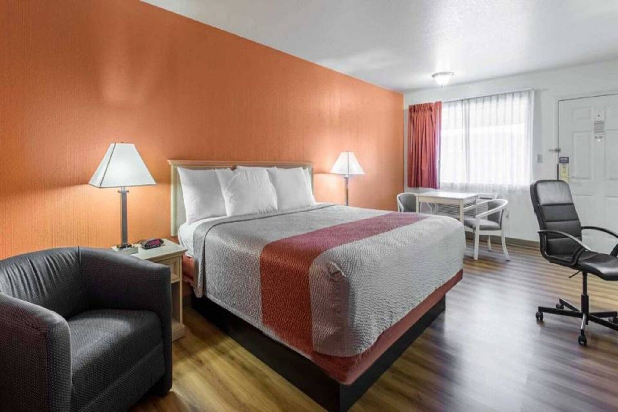Una habitación de hotel con cama, dos lámparas de noche, un escritorio con silla y una ventana con cortinas.