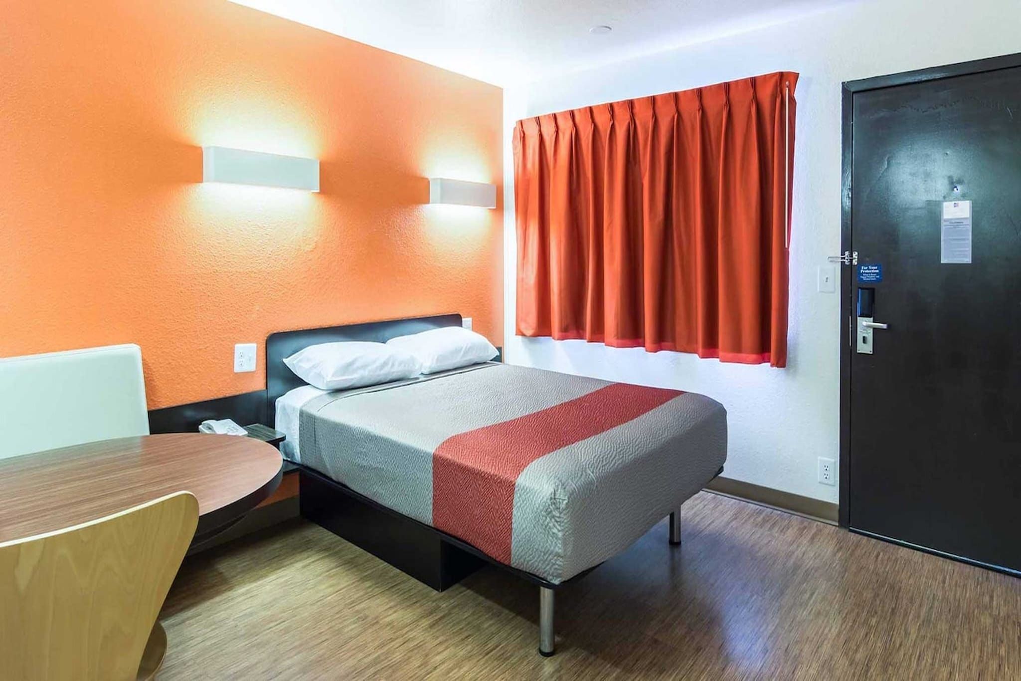 Une chambre d’hôtel avec un lit, un bureau, une chaise, une fenêtre avec des rideaux et une porte.