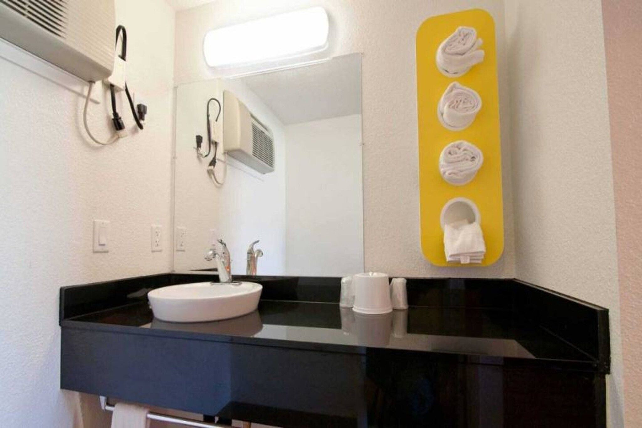 Une salle de bain moderne avec un plan de toilette noir, un lavabo blanc et un miroir. Des serviettes sont suspendues à un porte-serviettes jaune.