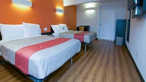 Een hotelkamer met twee bedden, een houten vloer en een deur naar een badkamer.
