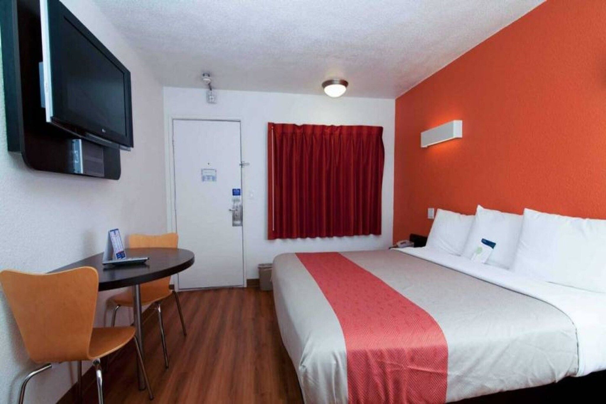 Une chambre d’hôtel avec un lit, un bureau, une chaise, une télévision et un rideau rouge.