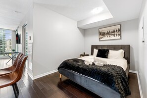 Une chambre d’hôtel moderne dotée d’un grand lit, offrant une vue sur la ville, et comprenant un coin repas avec des chaises.