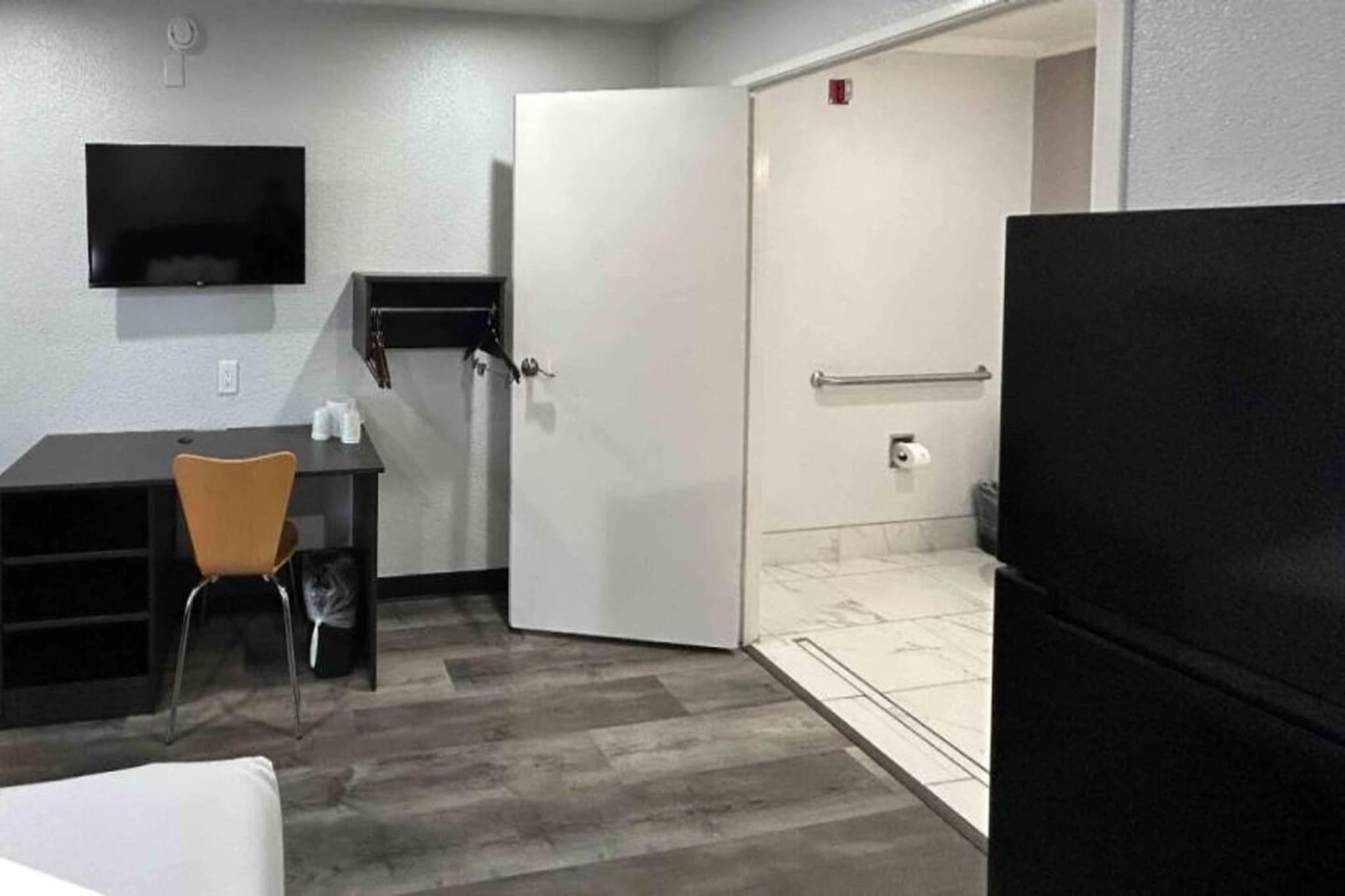 Een kleine kamer met een bureau, stoel en een zwarte koelkast.