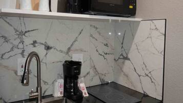 A kitchen with a sink, a coffee maker, and a microwave on a shelf.