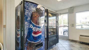 A vending machine with a Pepsi logo, located indoors with tiled flooring and a window showing a car outside.