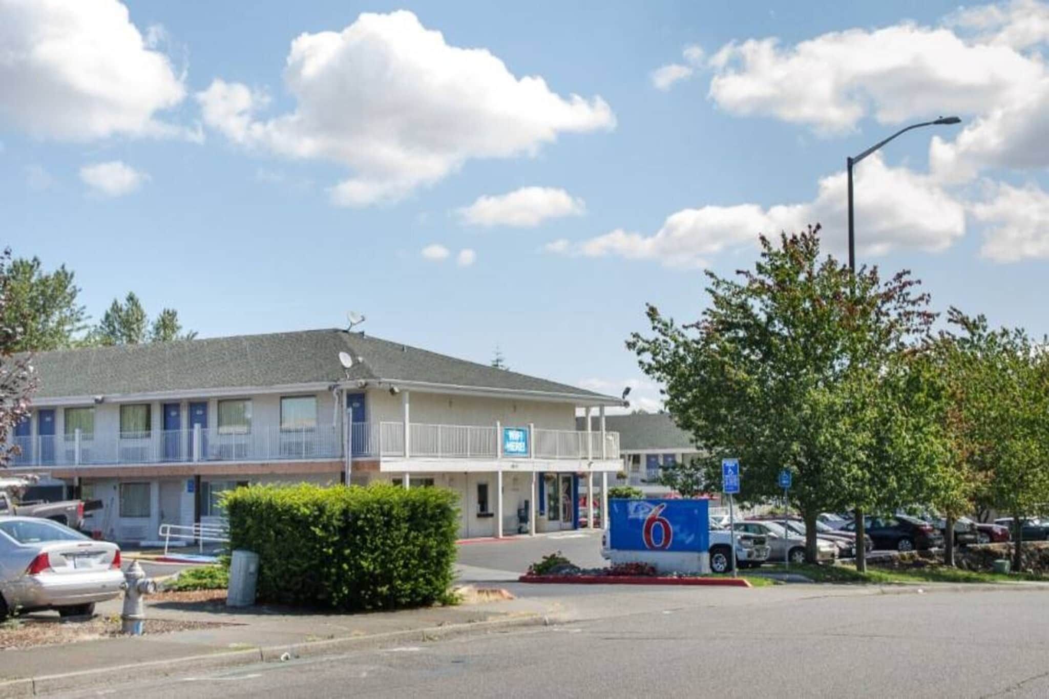 Un motel avec un parking, un panneau indiquant le numéro de chambre 6 et un lampadaire.