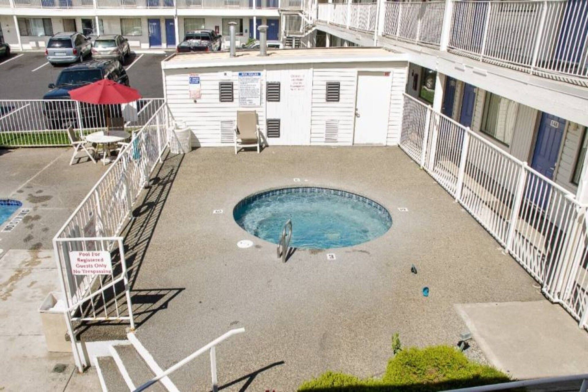 A rooftop pool area with a diving board, surrounded by a white railing, and a building in the background.