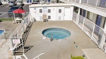A rooftop pool area with a diving board, surrounded by a white railing, and a building in the background.