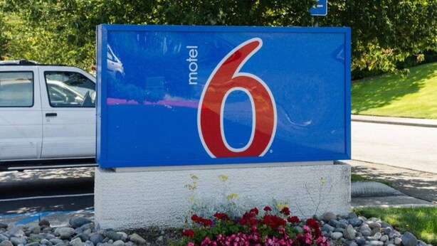 Cartell de motel amb el número 6, envoltat d'un llit de flors i una tanca.