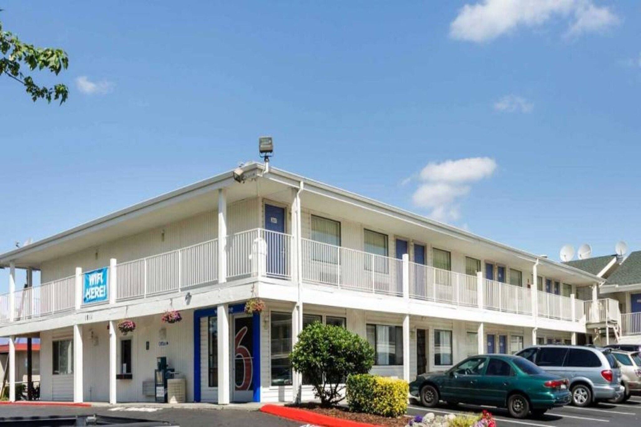 A two-story motel with a balcony on the second floor, a sign indicating WiFi availability, and a parking lot with several cars.