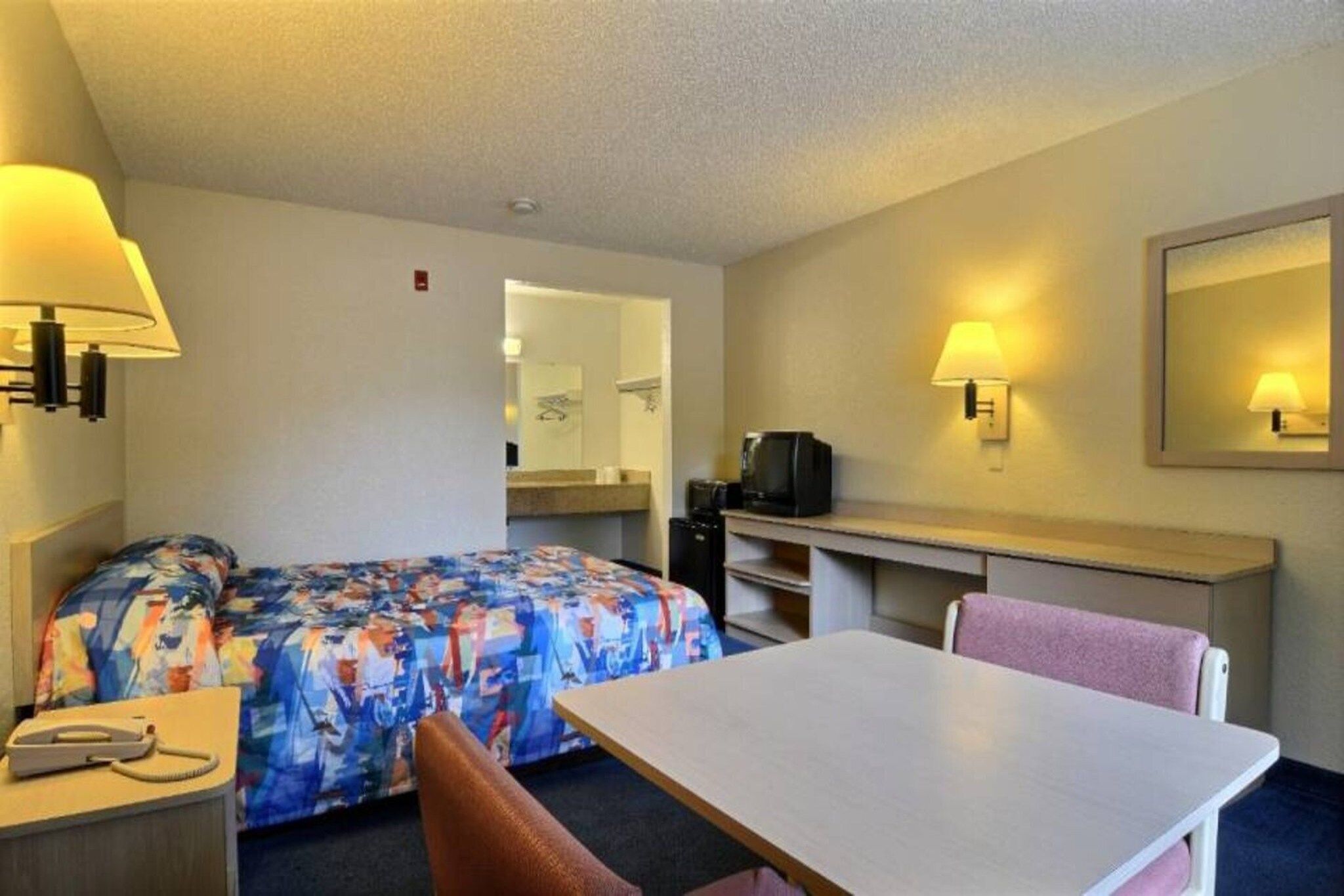 A hotel room with a bed, a desk, a chair, a telephone, and a television.