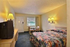 Une chambre d’hôtel avec un lit, un bureau avec un ordinateur, une chaise, une fenêtre avec des rideaux et une porte.