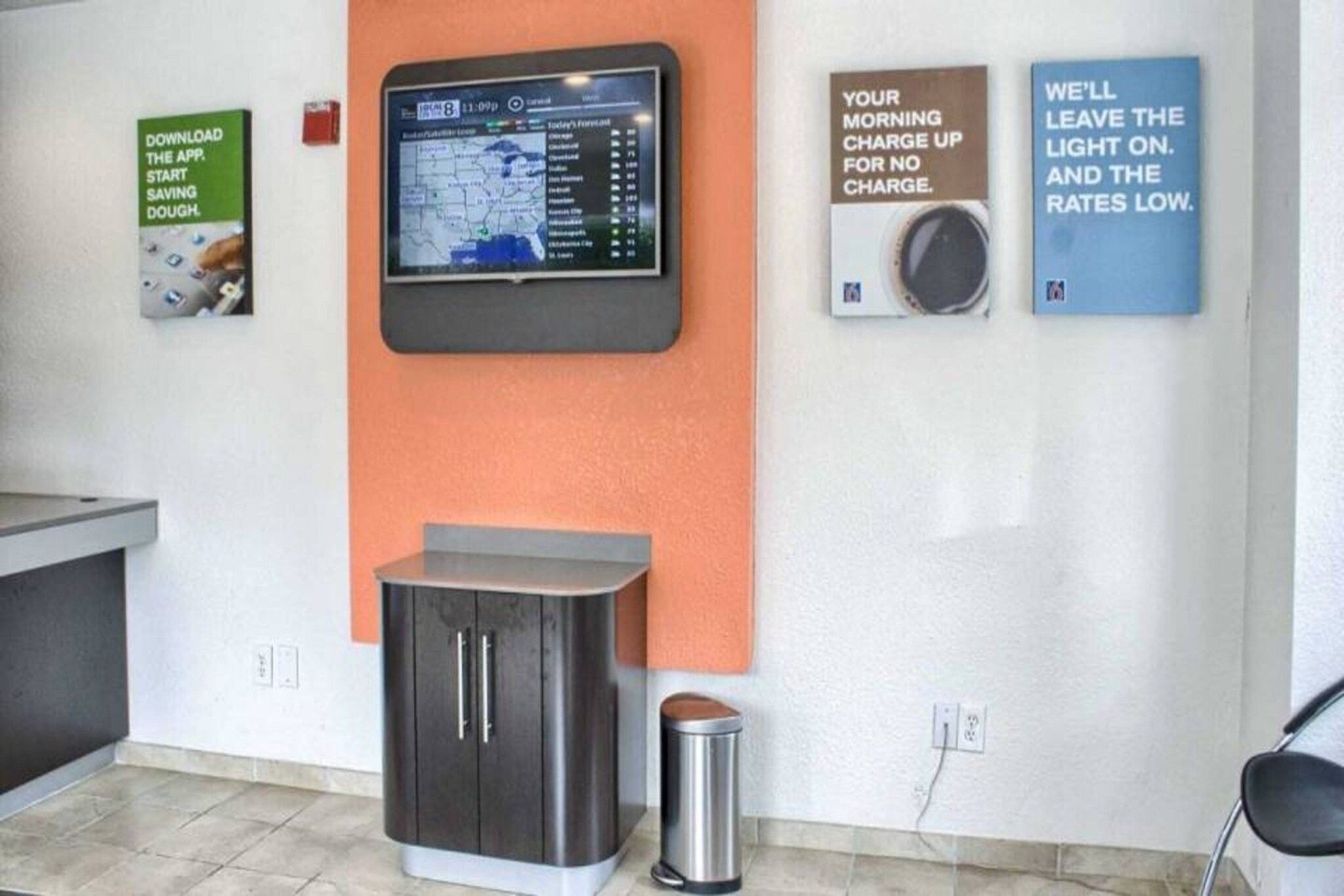 A room with a digital display, a trash bin, and two informational posters on the wall.