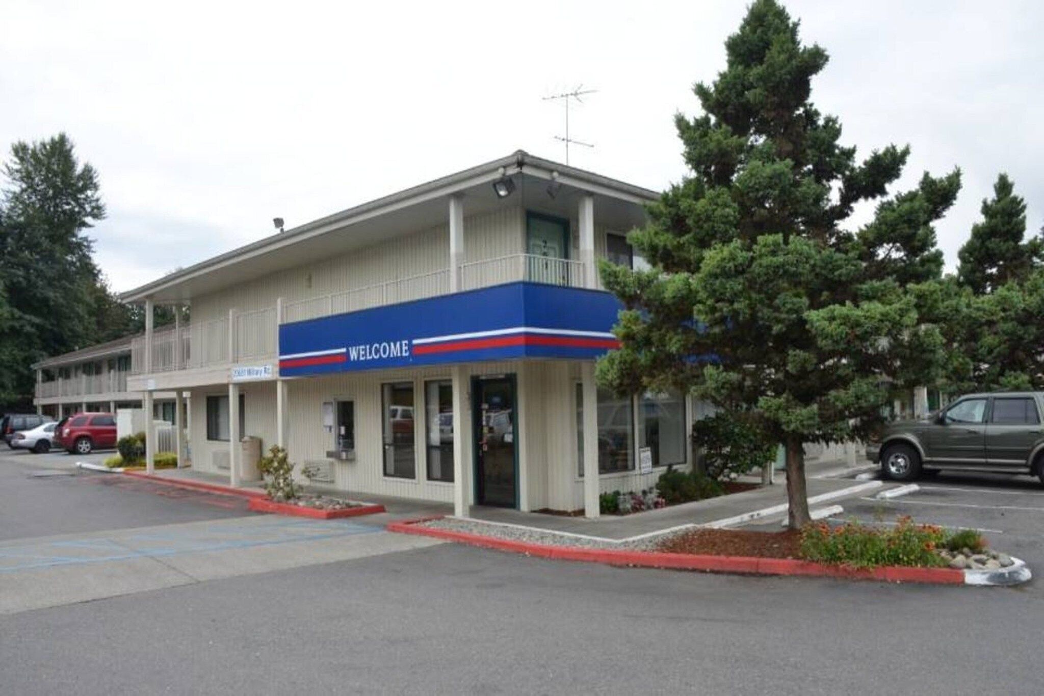 A two-story building with a 'WELCOME' sign, a parking lot, and a tree in front.