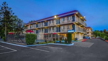 Un hôtel à plusieurs étages, avec une enseigne « Bienvenue », des places assises en plein air et un parking.