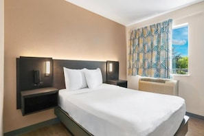 Ett hotellrum med en stor säng, två sängbord med lampor, ett fönster med mönstrade gardiner och en inbyggd luftkonditioneringsanläggning.