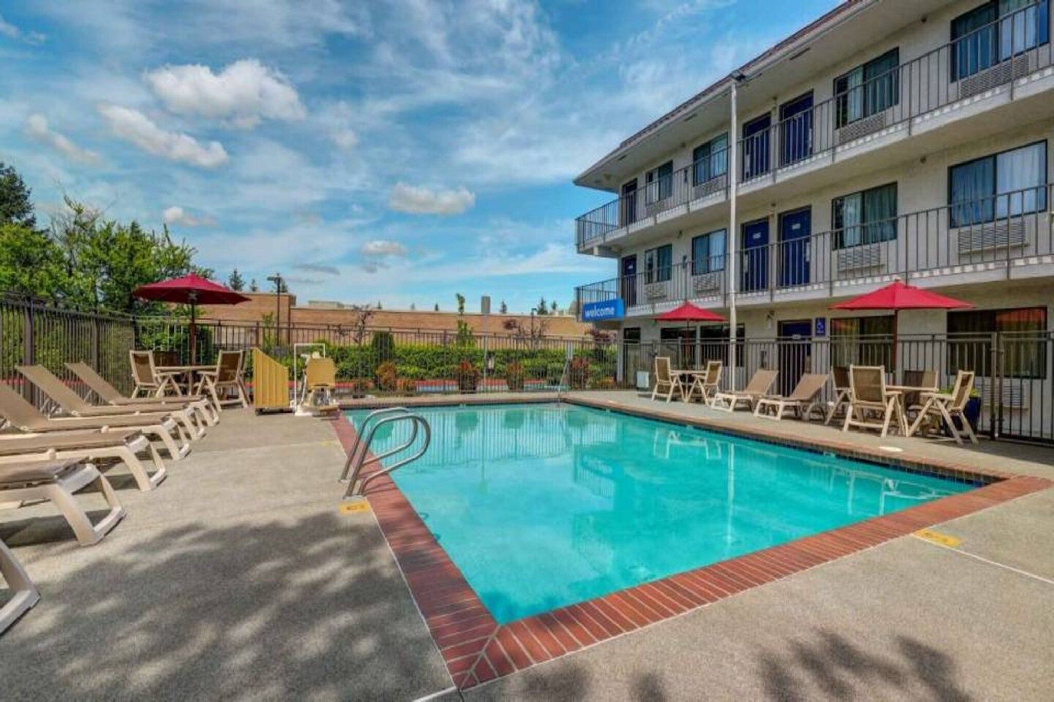 A swimming pool with lounge chairs and umbrellas, surrounded by a building with balconies.