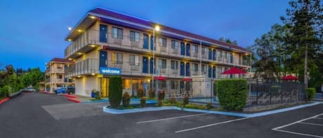 A multi-story hotel with a 'welcome' sign, outdoor seating, and a fenced parking area.