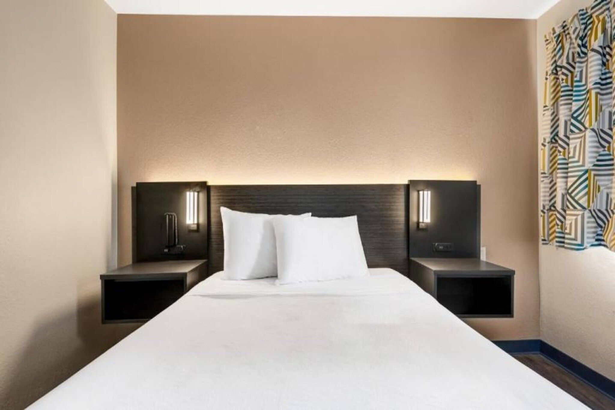 Een hotelkamer met een groot bed, twee nachtkastjes en een hoofdbord met ingebouwde verlichting.