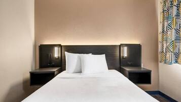 A hotel room with a large bed, two bedside tables, and a headboard with integrated lighting.