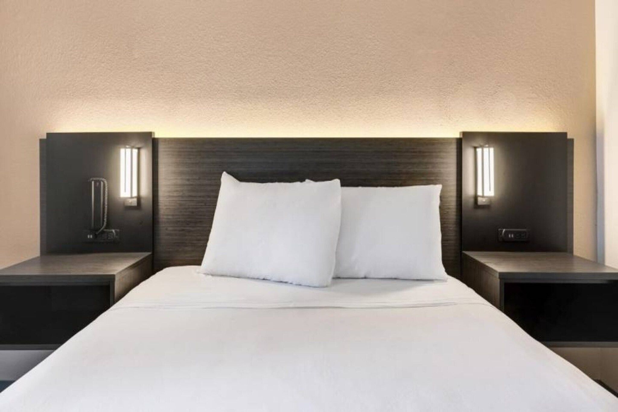 Une chambre d’hôtel moderne avec un grand lit, deux tables de chevet et des lampes de lecture fixées au mur.