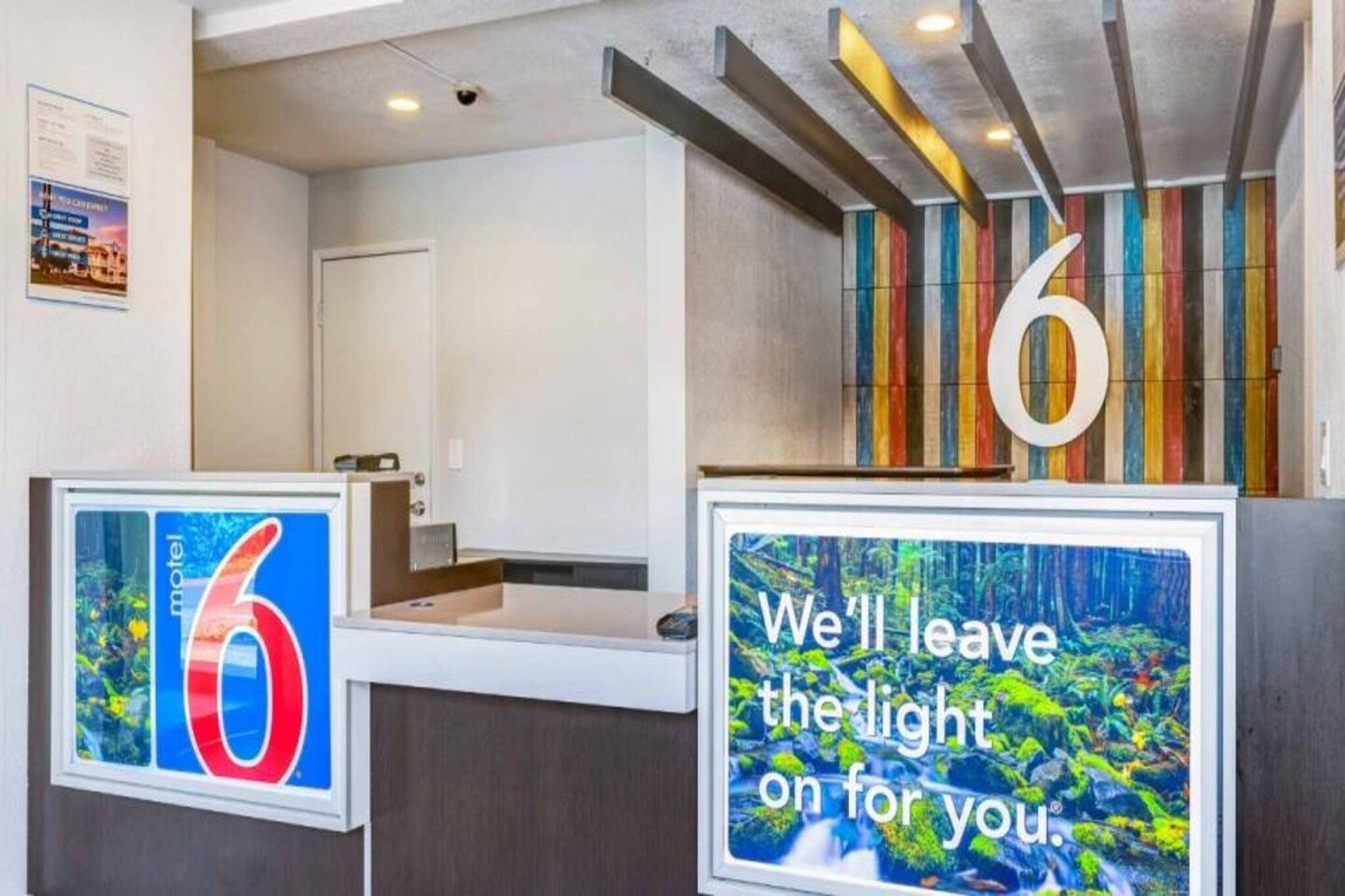 Ein Hotel-Rezeptionsschalter mit einem großen Schild mit der Zahl '6', einer gerahmten Willkommensbotschaft und einer farbenfrohen, gestreiften Wand im Hintergrund.