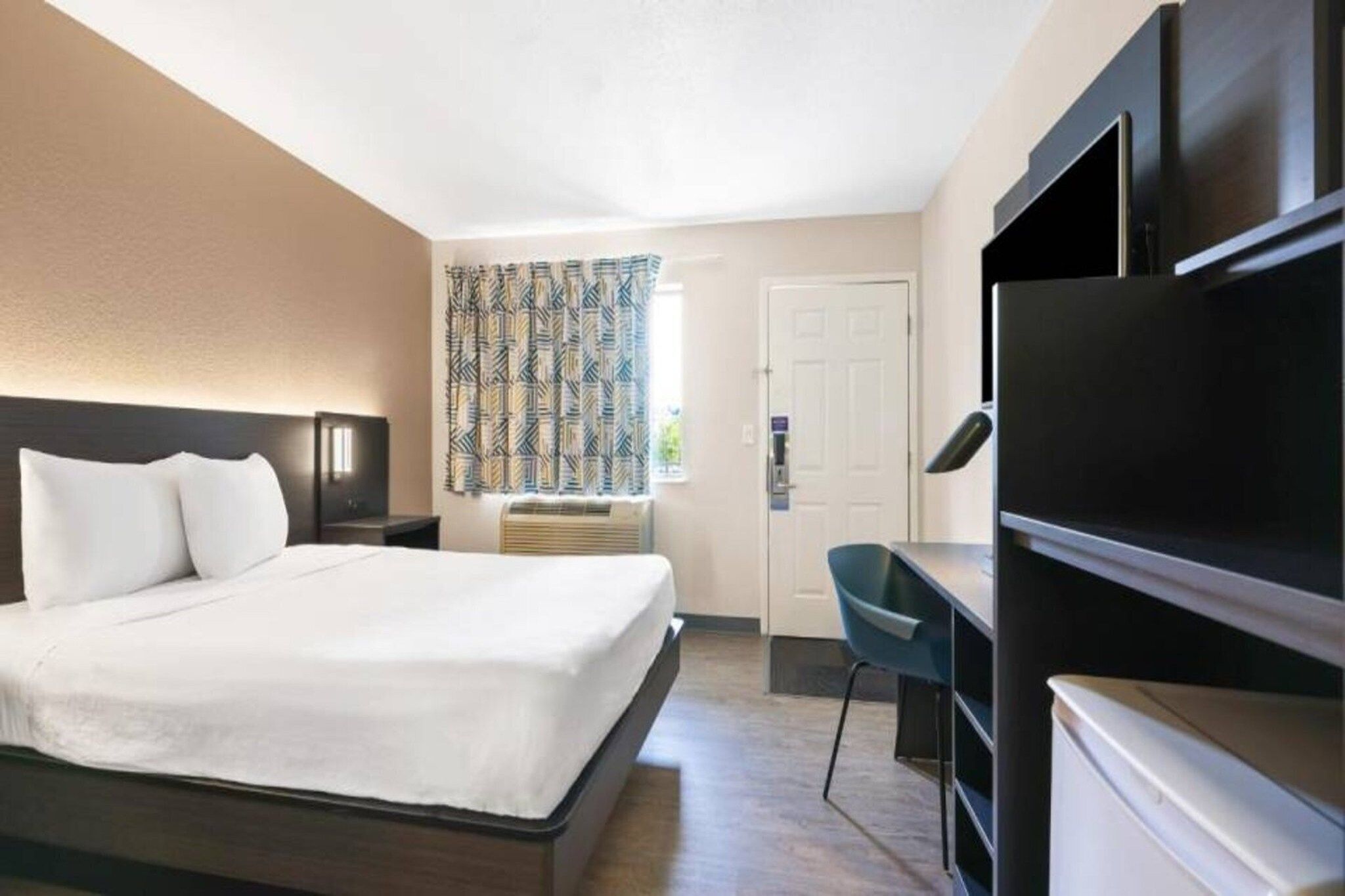 A hotel room with a bed, a desk, a chair, a television, and a door.