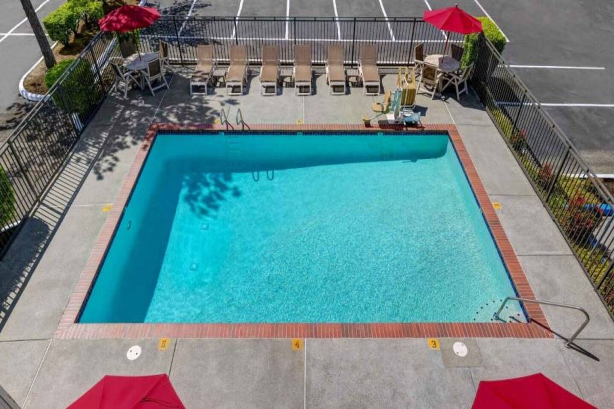 Une piscine rectangulaire dont le bord est recouvert de carrelage, et qui est entourée d’une clôture en métal.