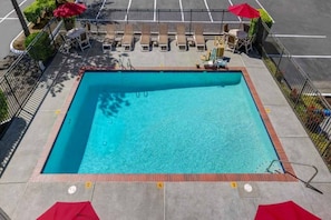 Une piscine rectangulaire dont le bord est recouvert de carrelage, et qui est entourée d’une clôture en métal.