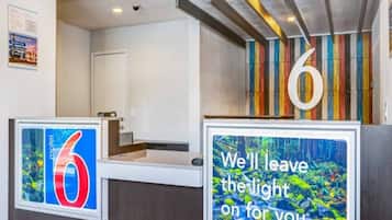 Un comptoir d’accueil d’hôtel avec un grand panneau portant le chiffre « 6 », un message de bienvenue encadré et un mur coloré à rayures en arrière-plan.