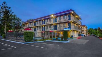 Un hôtel à plusieurs étages, avec une enseigne « Bienvenue », des places assises en plein air et un parking.
