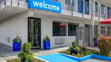A building with a 'welcome' sign, a gated entrance, and a landscaped area with plants and a small pool.