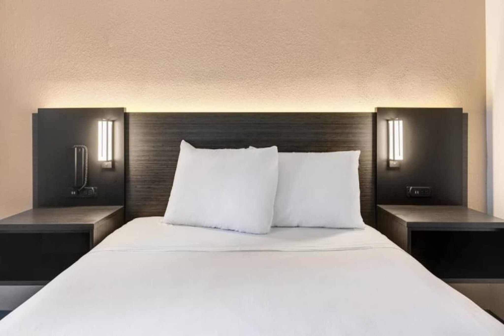 Ett modernt hotellrum med en stor säng, två sängbord och väggmonterad belysning.