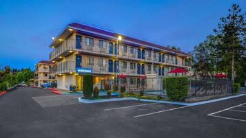 Un hôtel à plusieurs étages, avec une enseigne indiquant « Bienvenue », des places assises à l’extérieur et un espace de stationnement clôturé.