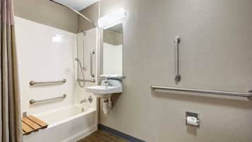 Une salle de bain équipée d’une baignoire, d’un lavabo, d’un miroir et de toilettes. Des barres d’appui sont installées à proximité du lavabo et des toilettes.