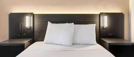 A modern hotel room with a large bed, two bedside tables, and wall-mounted lighting.