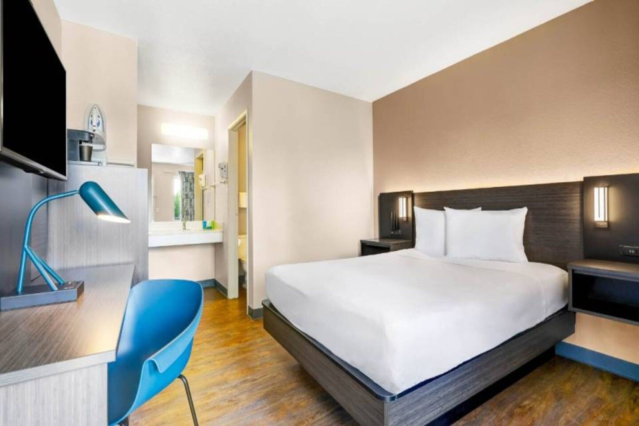 Een hotelkamer met een bed, nachtkastjes, een bureau met een lamp, een stoel en een televisie.