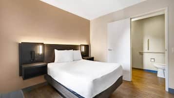 Une chambre d’hôtel avec un grand lit, des tables de chevet, une petite table et une salle de bain visible à travers une porte ouverte.