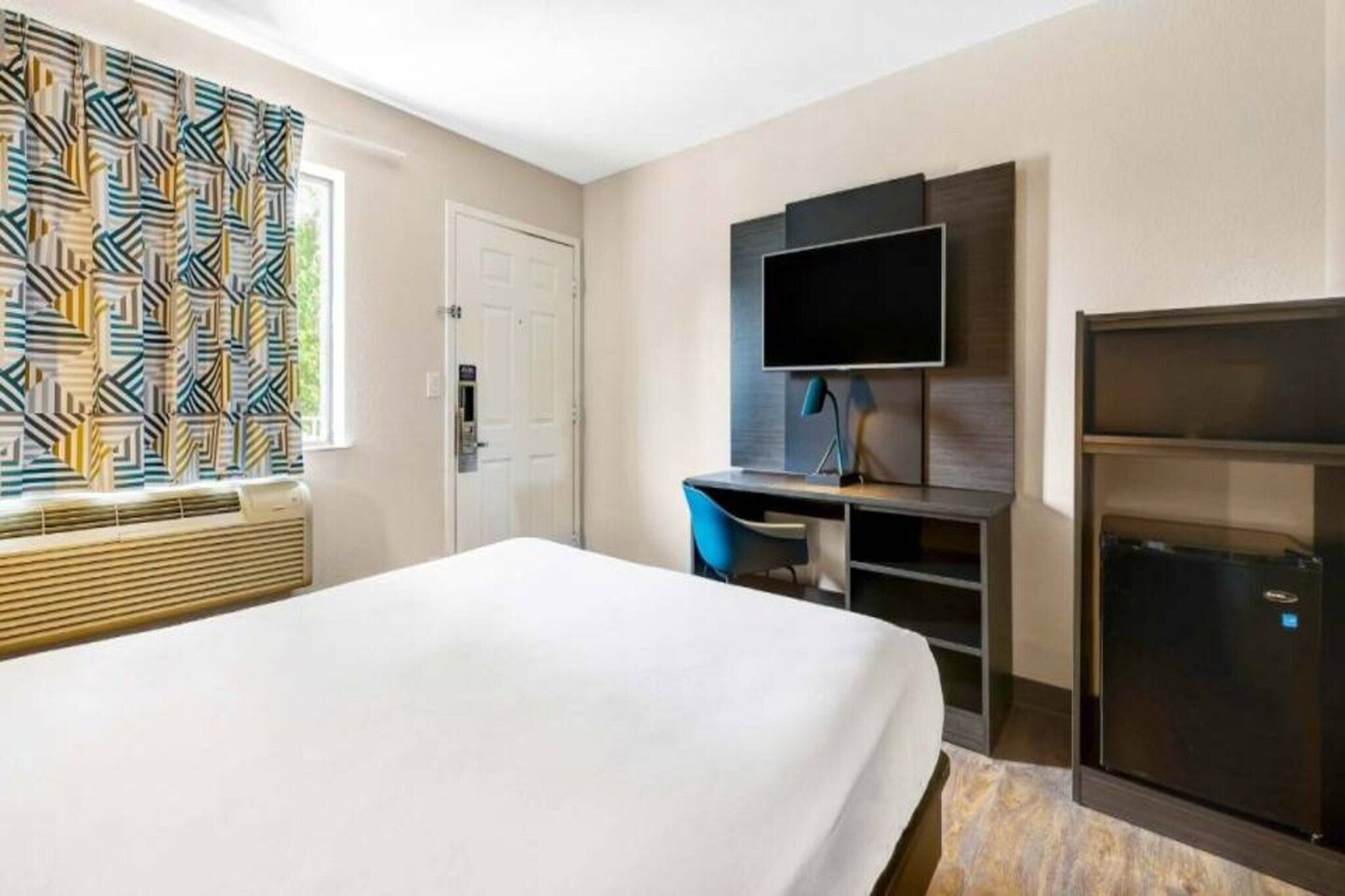 Een hotelkamer met een bed, een bureau met een computer, een televisie en een minibar.