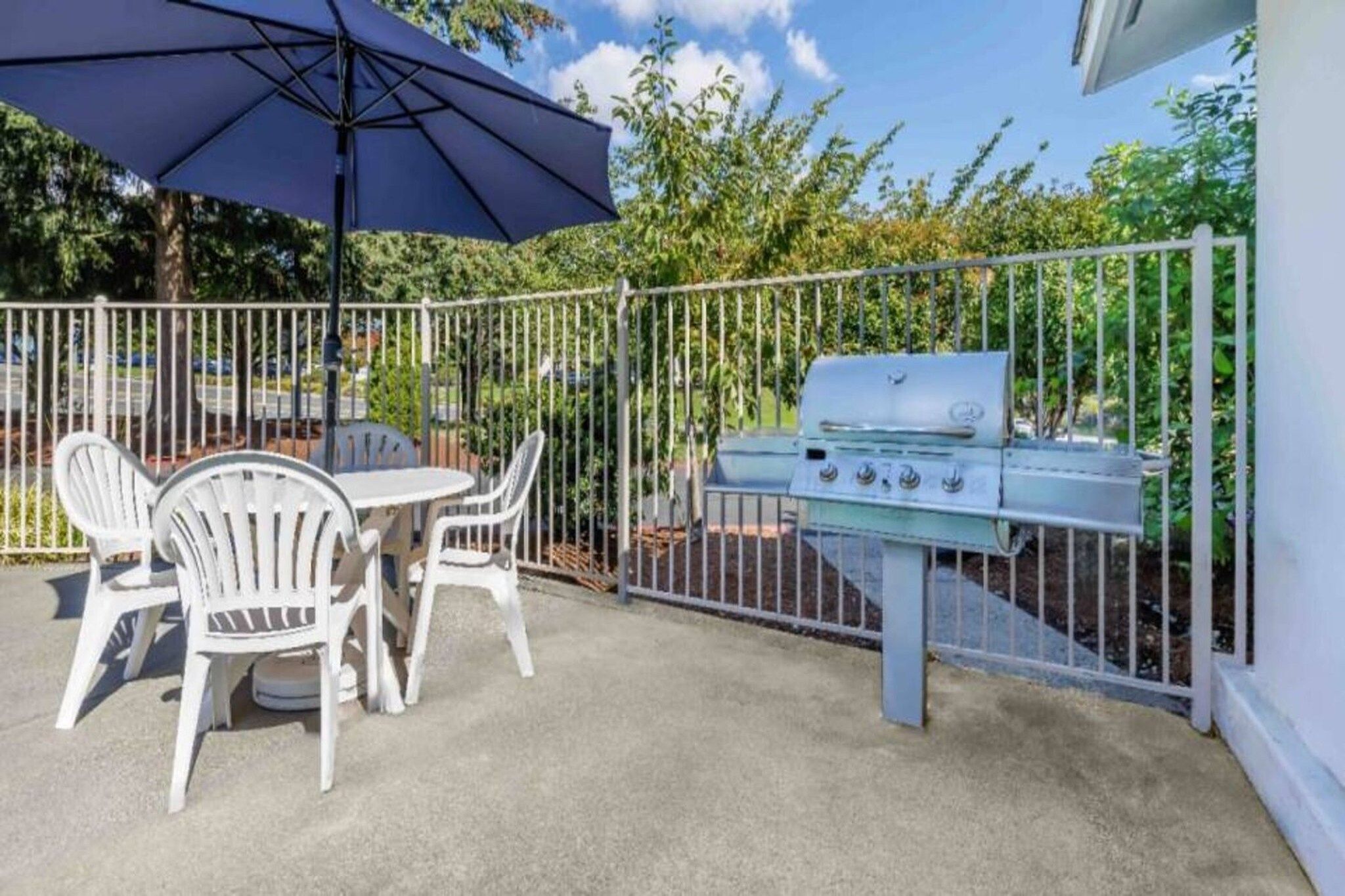 An outdoor patio with a grill, white chairs, and a table.