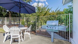 Une terrasse extérieure avec un barbecue, des chaises blanches et une table.