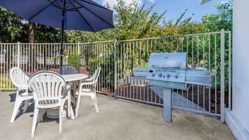 An outdoor patio with a grill, white chairs, and a table.